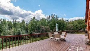A wooden deck with outdoor furniture and a view of a forest. - Alaska Grizzly Lodge (Fairbanks)