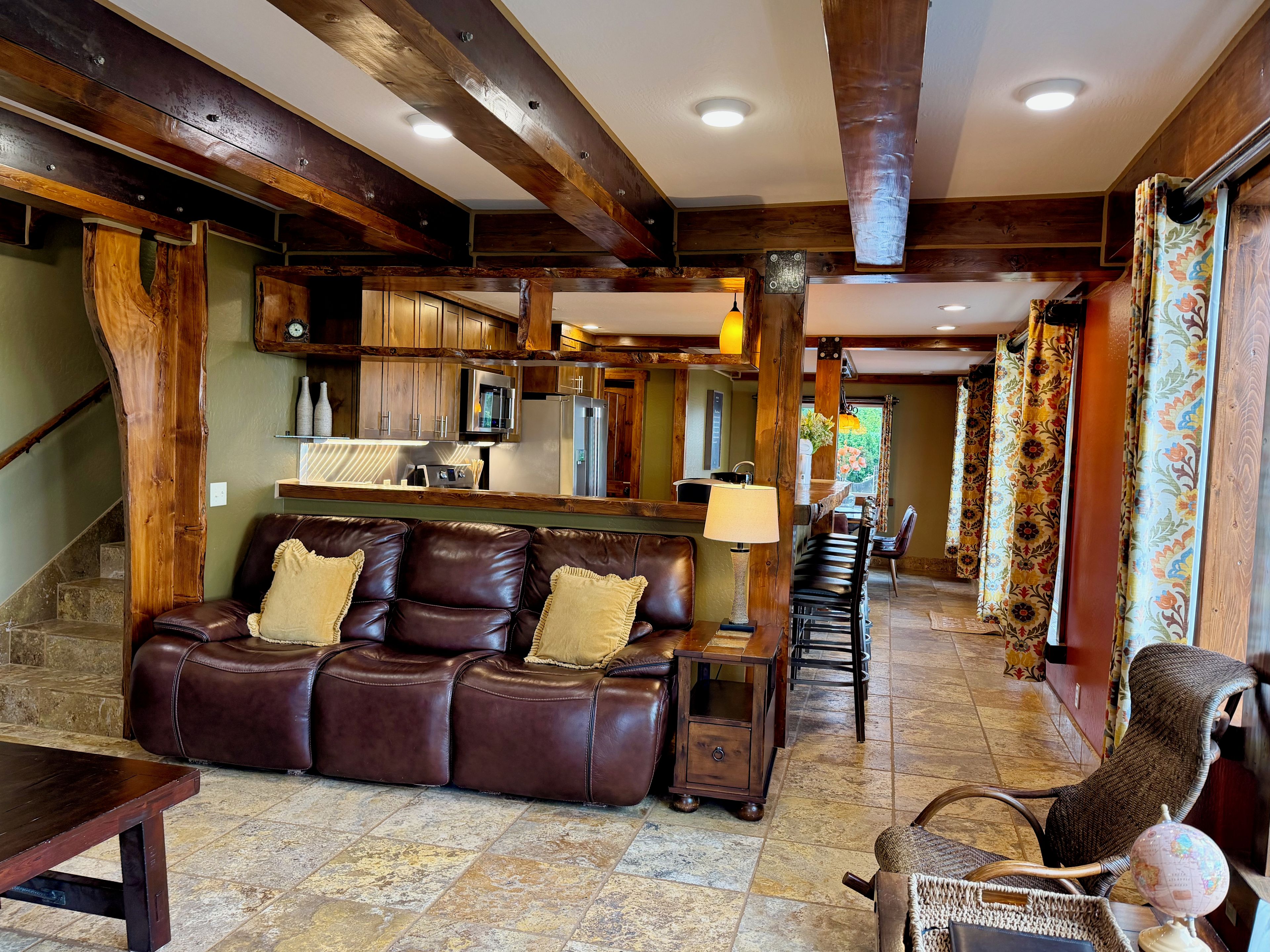 A spacious living area with a leather sofa, a wooden coffee table, and a wicker chair with a globe. A kitchen with modern appliances is visible in the background.