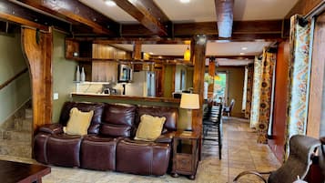 A spacious living area with a leather sofa, a wooden coffee table, and a wicker chair with a globe. A kitchen with modern appliances is visible in the background.