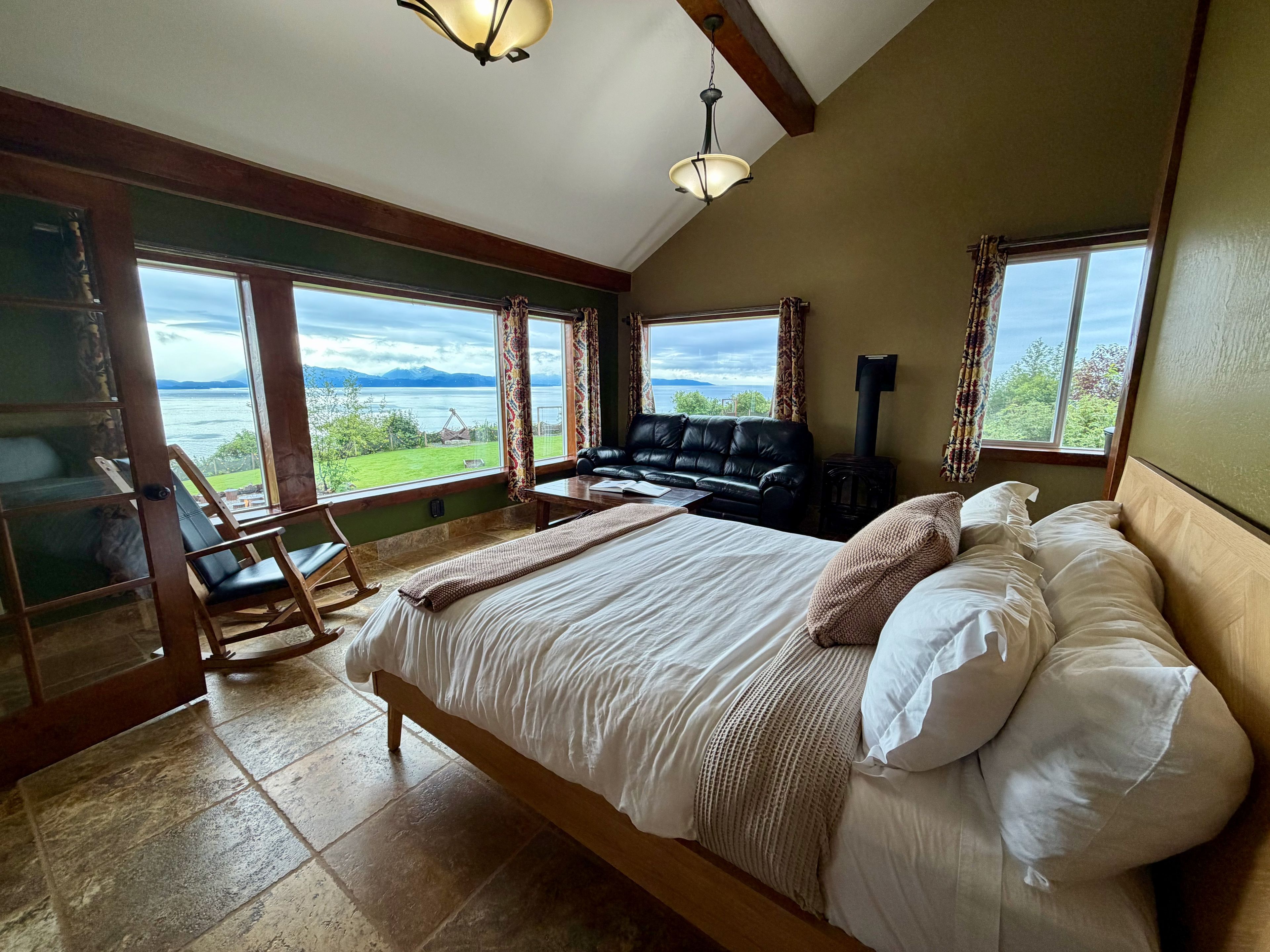 A bedroom with a large bed, a sofa, a fireplace, and a view of the outdoors.