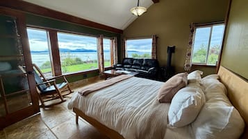 A bedroom with a large bed, a sofa, a fireplace, and a view of the outdoors.