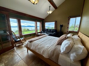 A bedroom with a large bed, a sofa, a fireplace, and a view of the outdoors. - Baycrest Lodge (Homer)