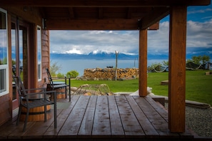 A wooden deck with chairs and a view of a lake and mountains. - Baycrest Lodge (Homer)