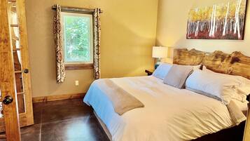 A bedroom with a bed, a window with curtains, a painting on the wall, and a wooden headboard.