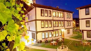 Un edificio de estilo europeo tradicional con varios pisos, un patio con mesas al aire libre y una entrada bien iluminada.
