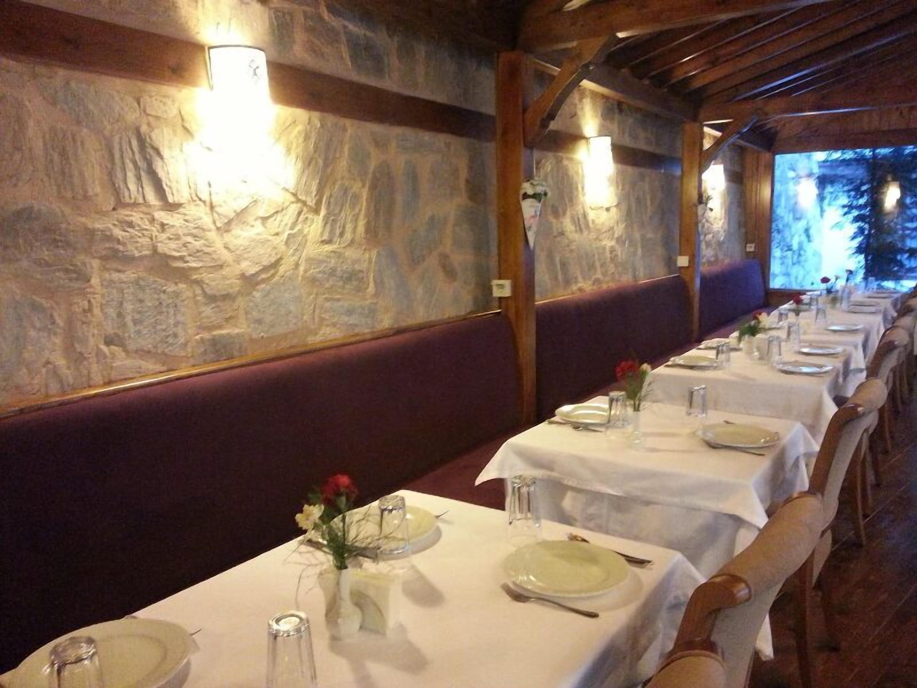 Una larga mesa de comedor dispuesta con manteles blancos, platos y cubiertos, flanqueada por paredes de piedra y vigas de madera.