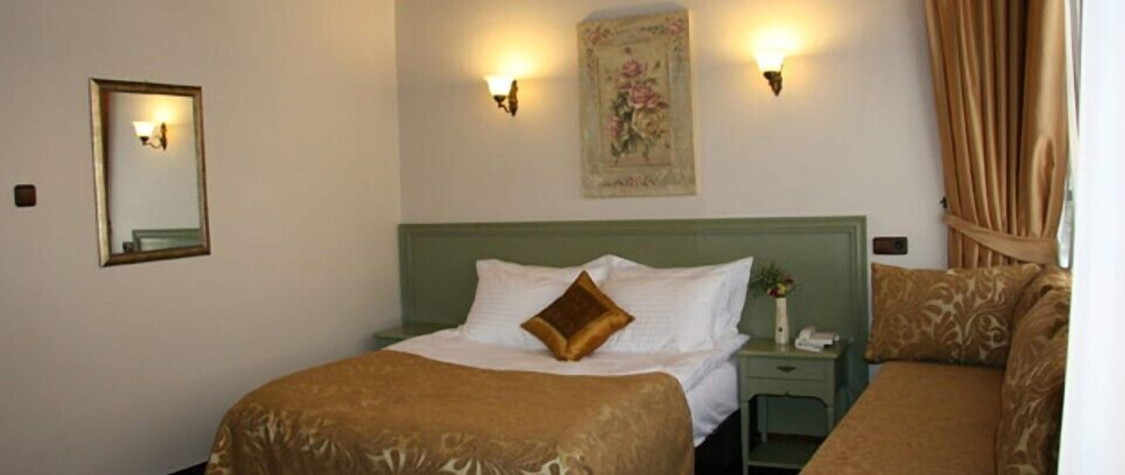 A hotel room with a green headboard, a bed with a brown bedspread, a nightstand with a phone, and a wall-mounted light fixture.