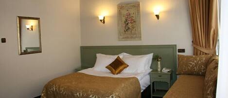 A hotel room with a green headboard, a bed with a brown bedspread, a nightstand with a phone, and a wall-mounted light fixture.