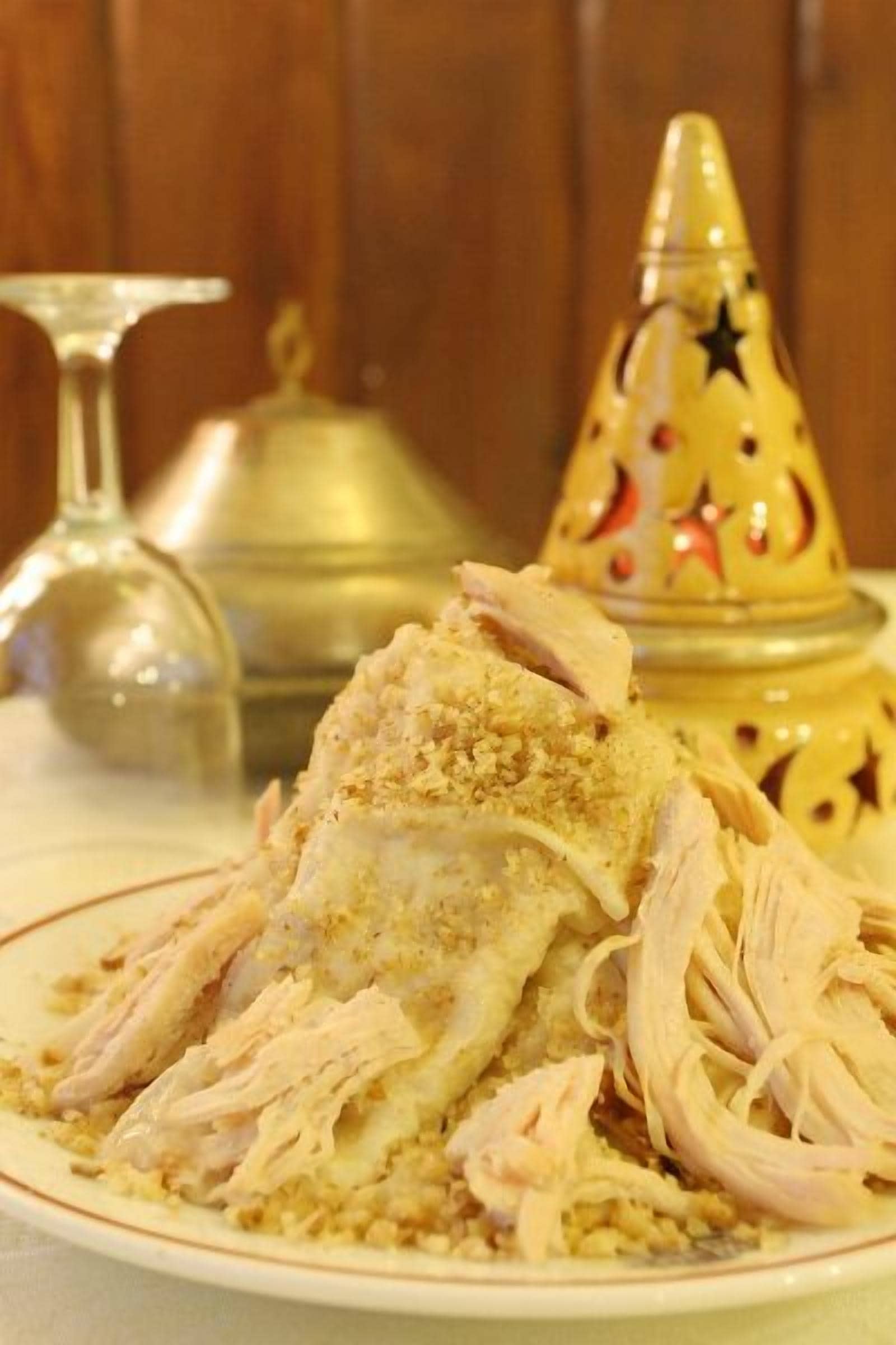 A plate of shredded chicken with a crumbly topping, a brass candlestick, and a decorative brass container with star patterns.
