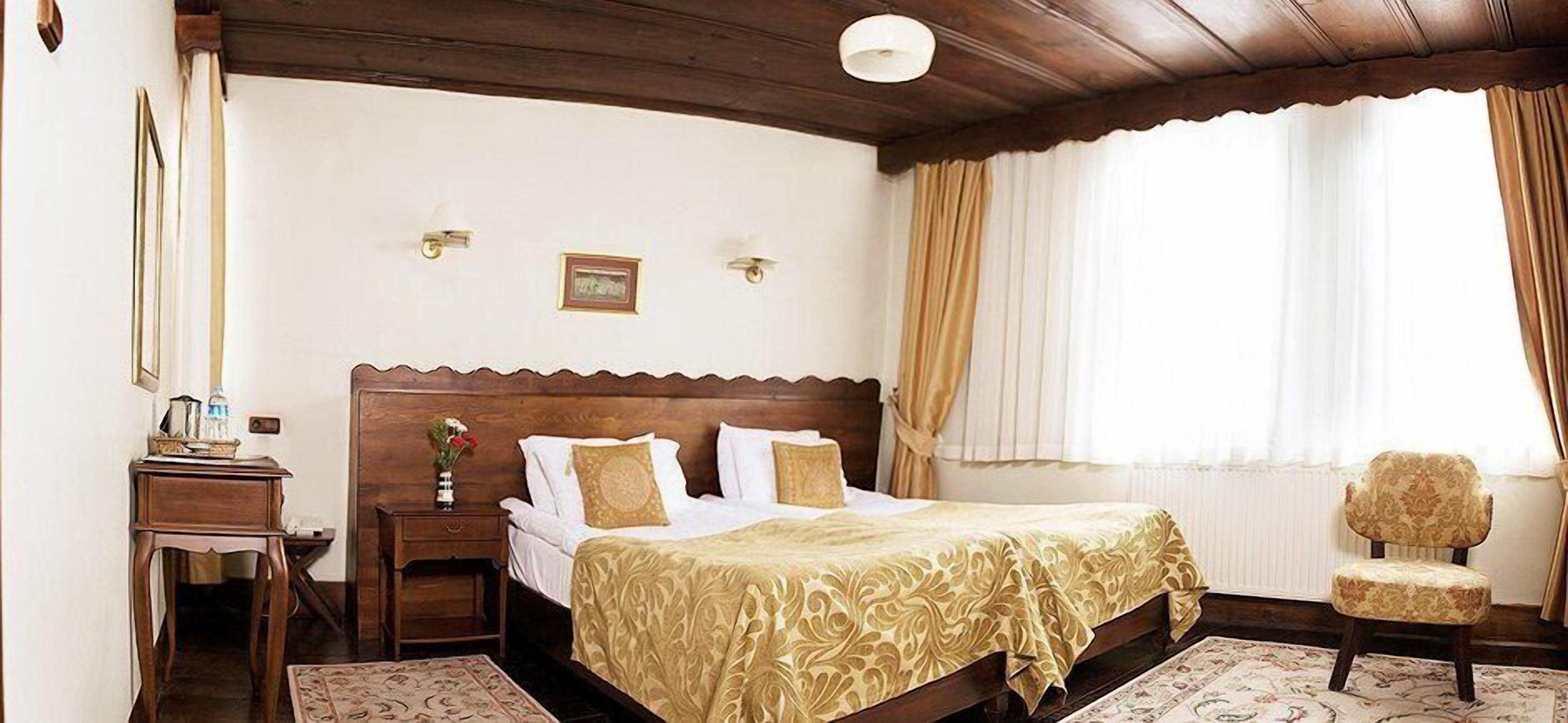 A hotel room with a wooden bed, a nightstand, a chair, and a window with curtains.