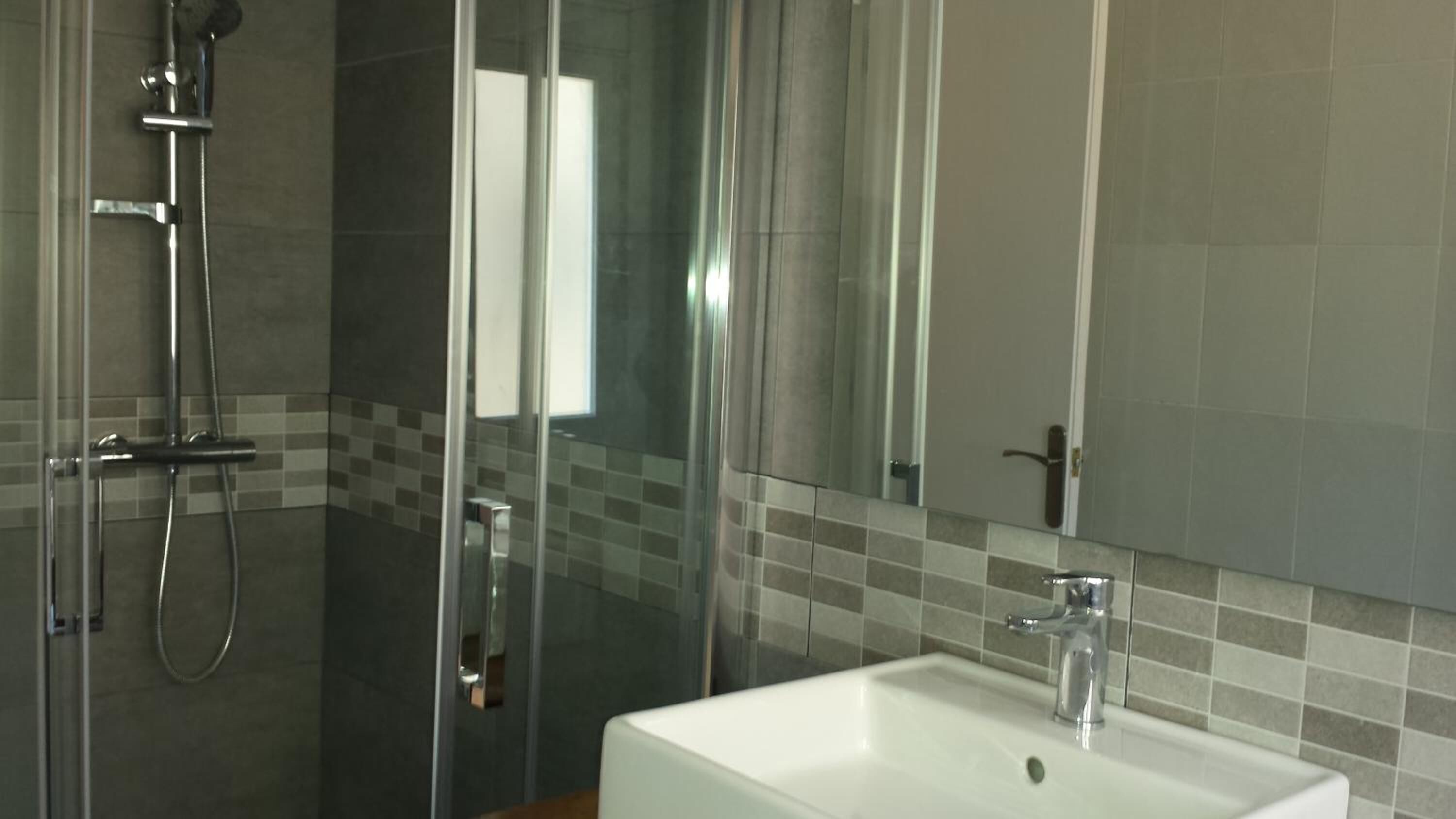 A modern bathroom with a glass shower enclosure, a white sink, and a large mirror.