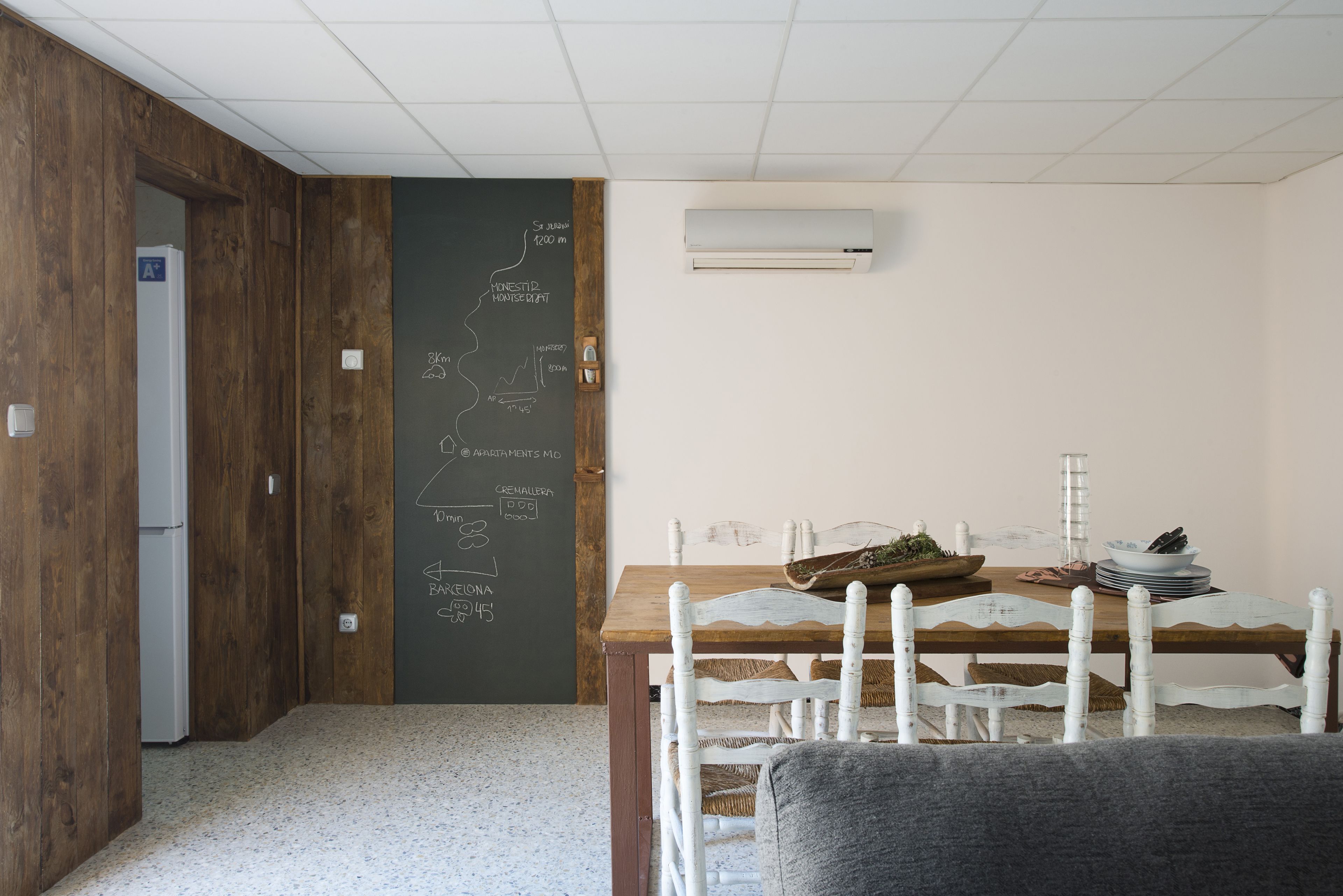 A room with a wooden floor, a white chair, a wooden table, and a chalkboard with text.