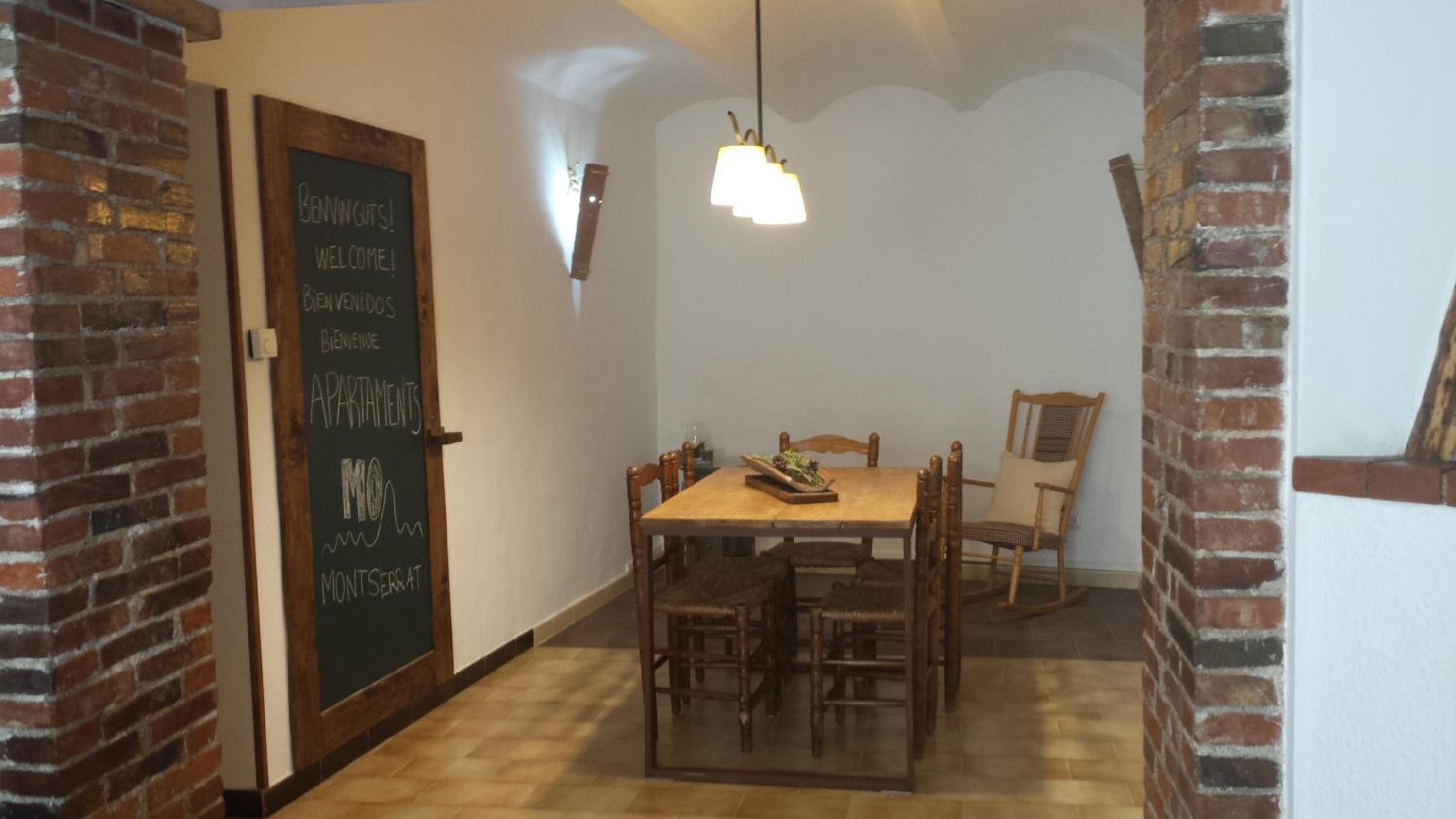 Een eetgedeelte met een houten tafel en stoelen, een prikbord met meer talige welkomstboodschappen en een hanglamp.