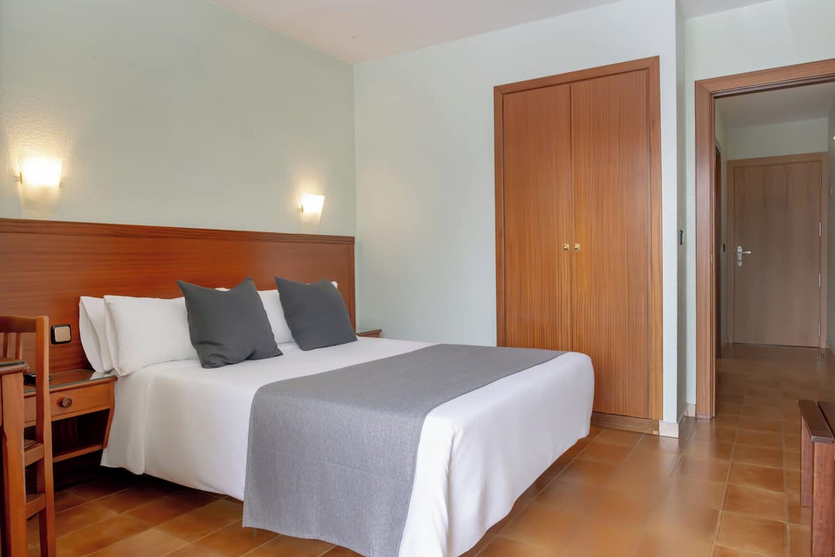 A hotel room with a bed, bedside tables, a wardrobe, and a wall-mounted light fixture.