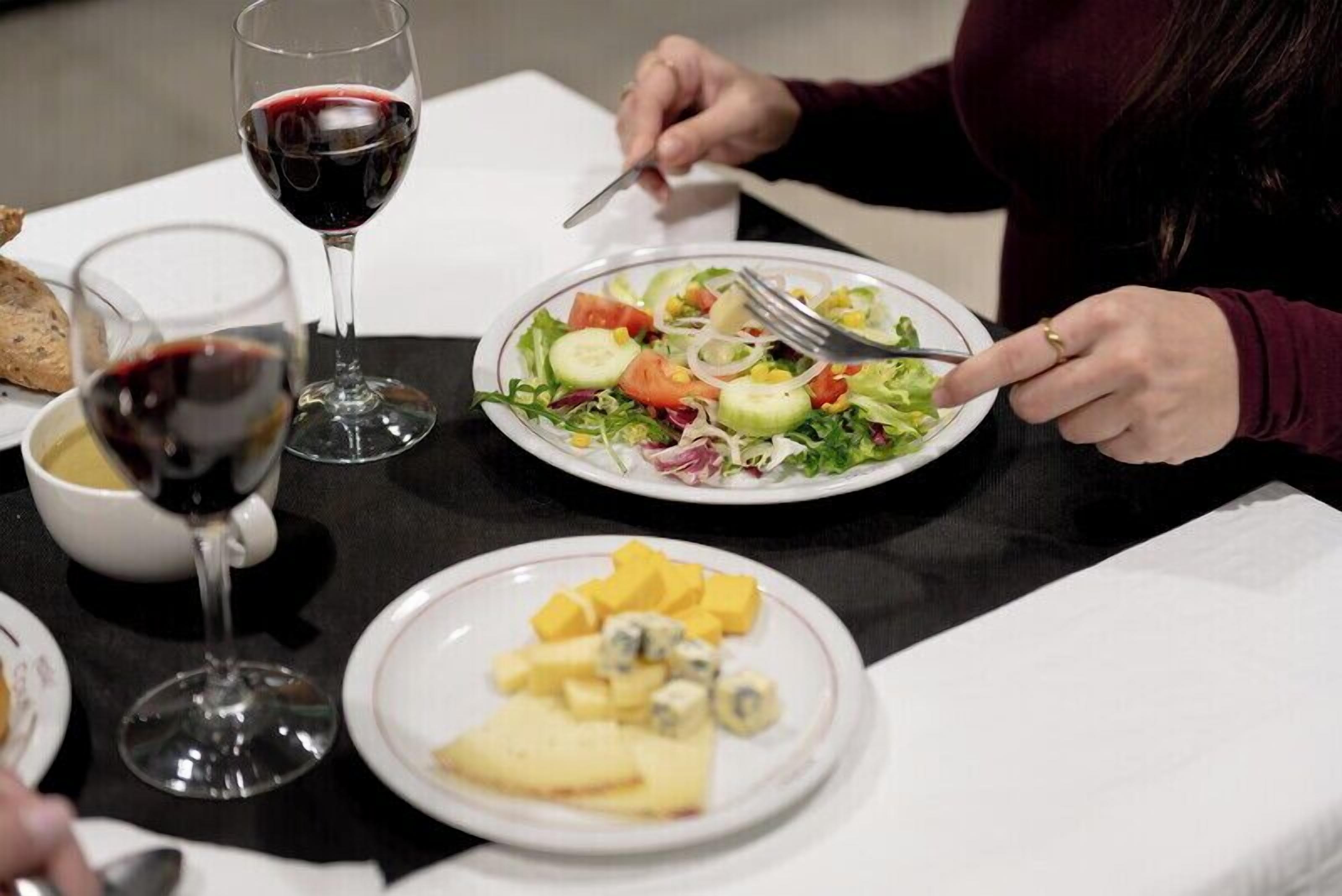 Une table à manger avec des assiettes remplies de nourriture, des verres à vin et une personne qui mange.