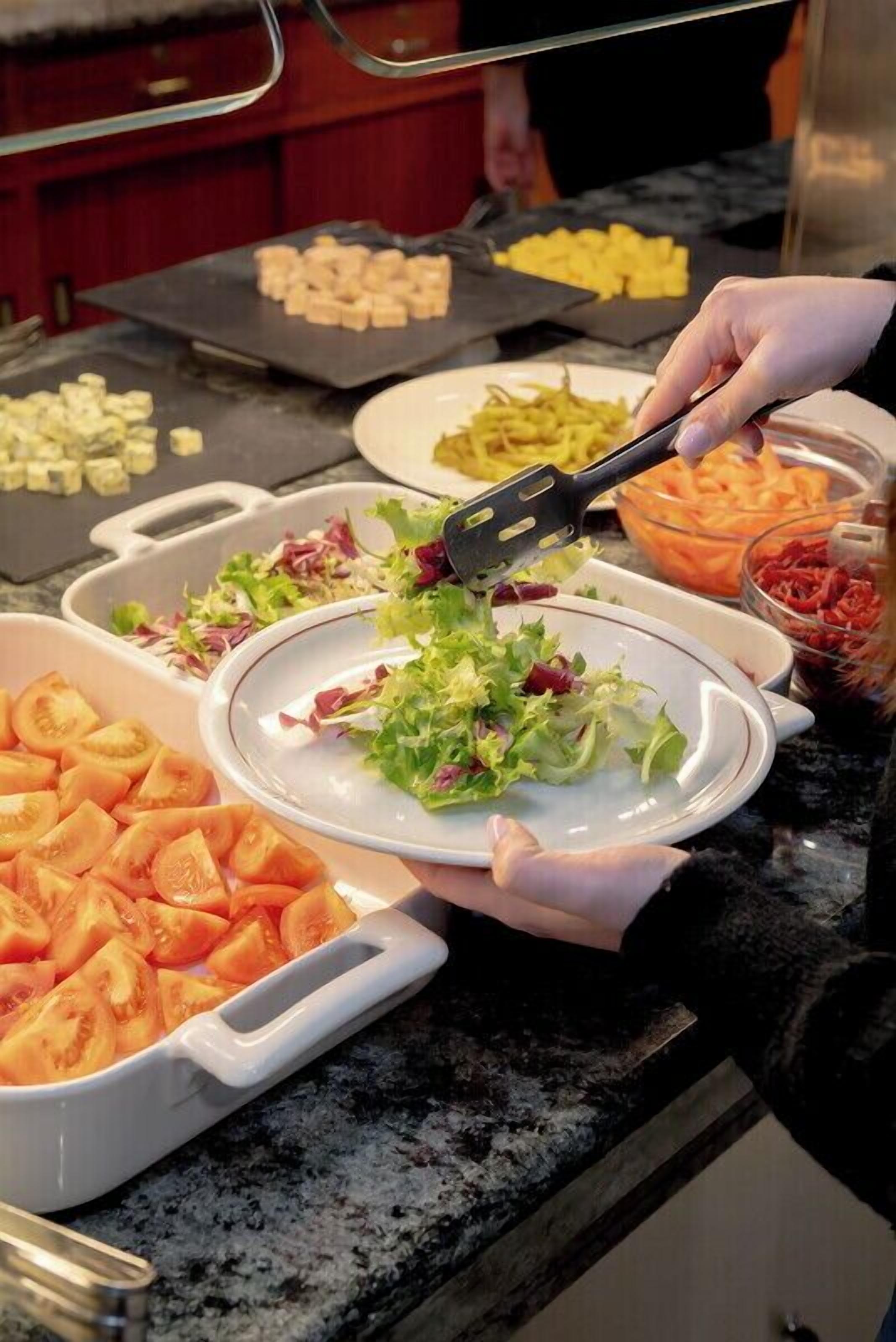 Una barra libre con distintos alimentos, como rodajas de tomate, ensalada y queso.