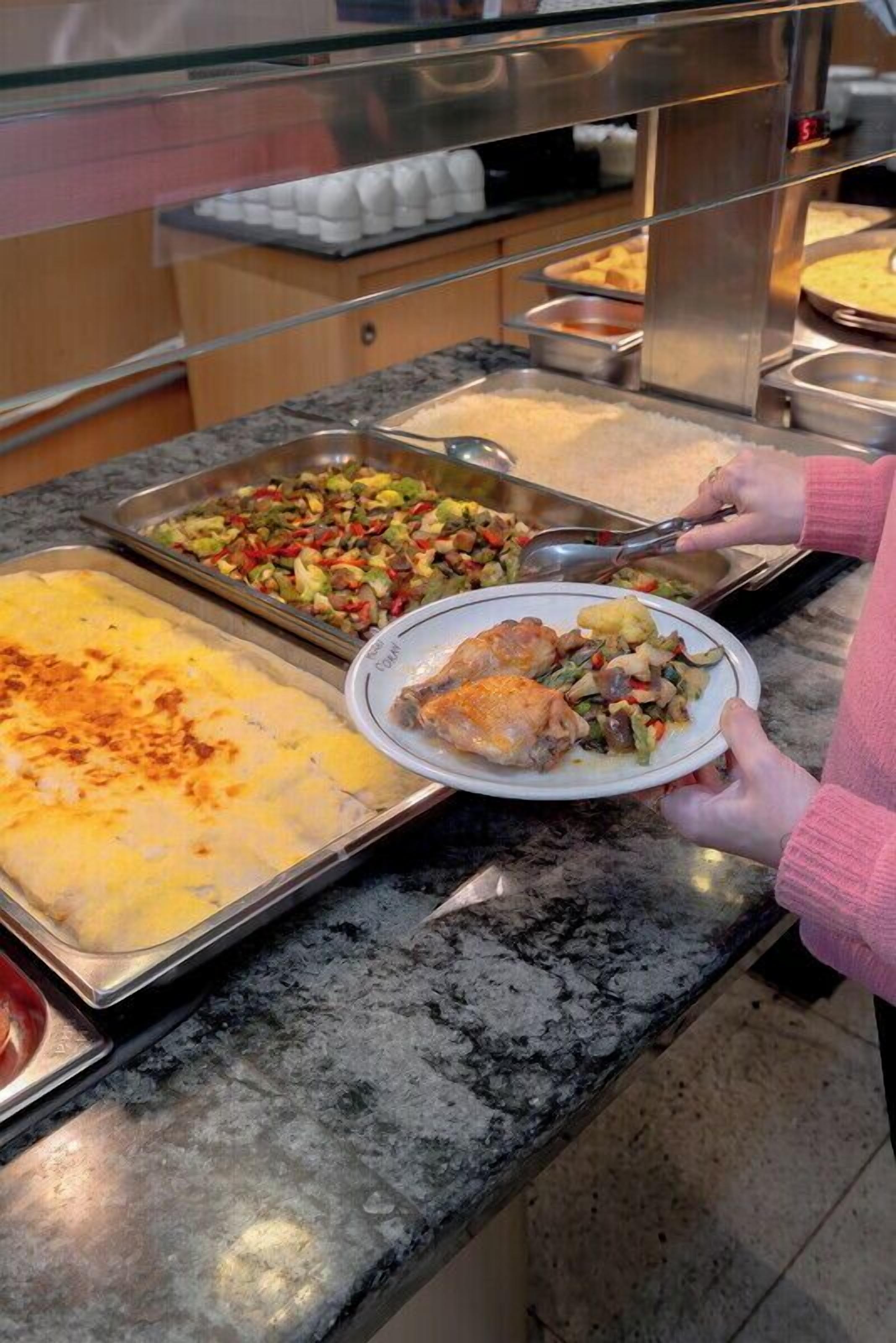 Ein reichhaltiges Buffet mit verschiedenen Speisen, darunter eine Platte mit gebackenen Kartoffeln, Hähnchen und Gemüse sowie ein Salat.
