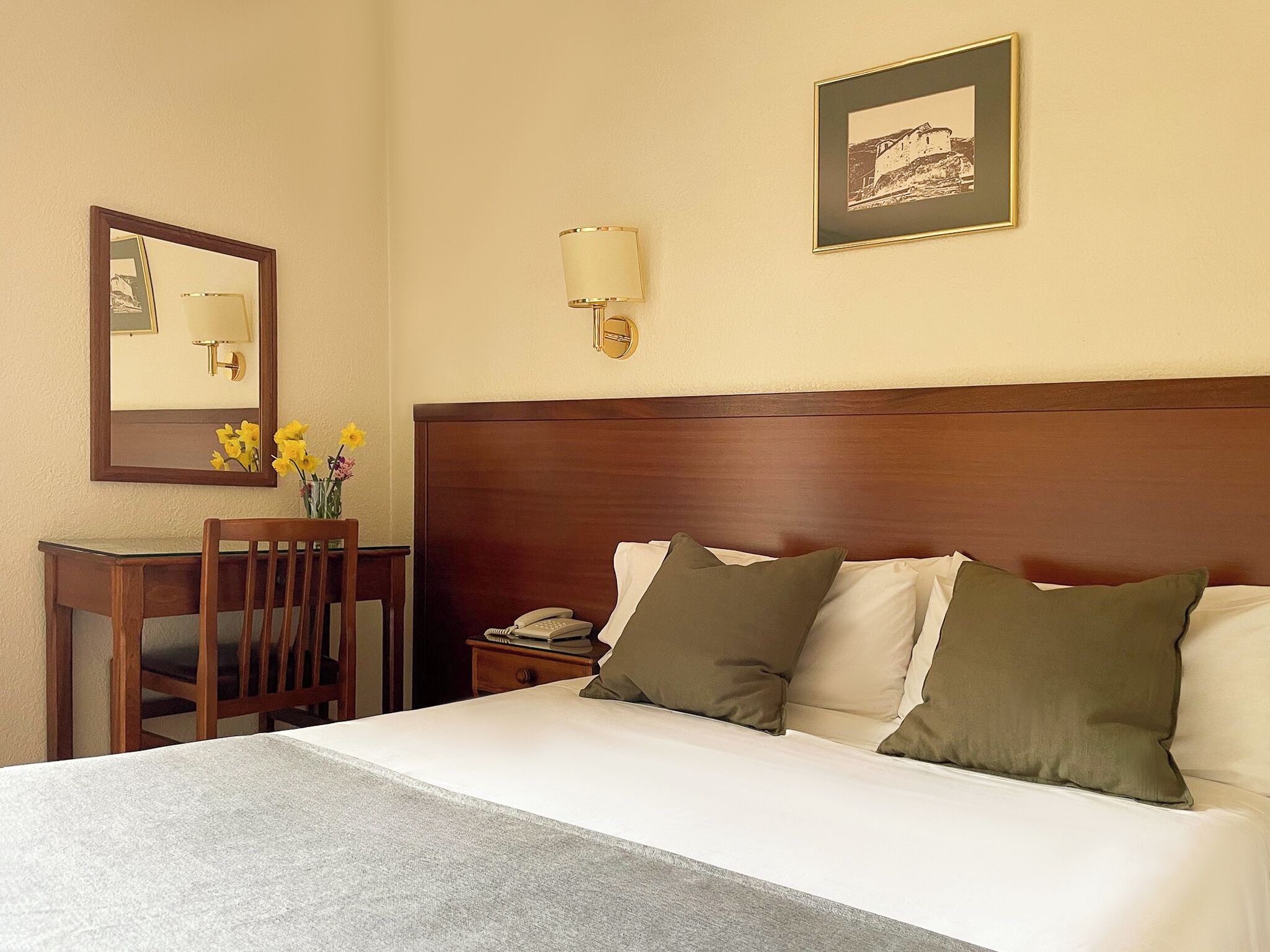 A hotel room with a bed, a desk, a chair, a lamp, and a framed picture on the wall.