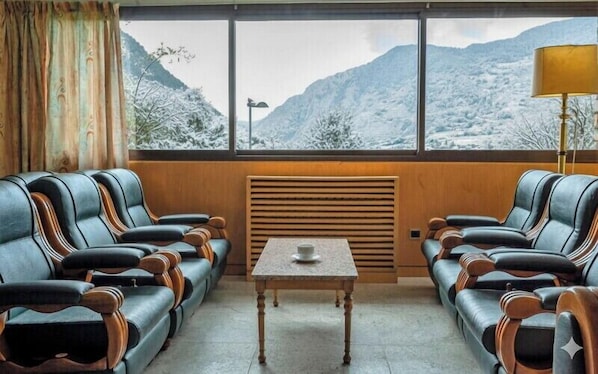 A room with two leather sofas facing a table, a window with a view of snow-covered mountains, and a lamp on the right.