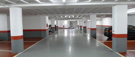 Un estacionamiento con varios niveles, con pilares blancos y detalles en rojo, que presenta un piso limpio y reflectante, y un pasillo central.