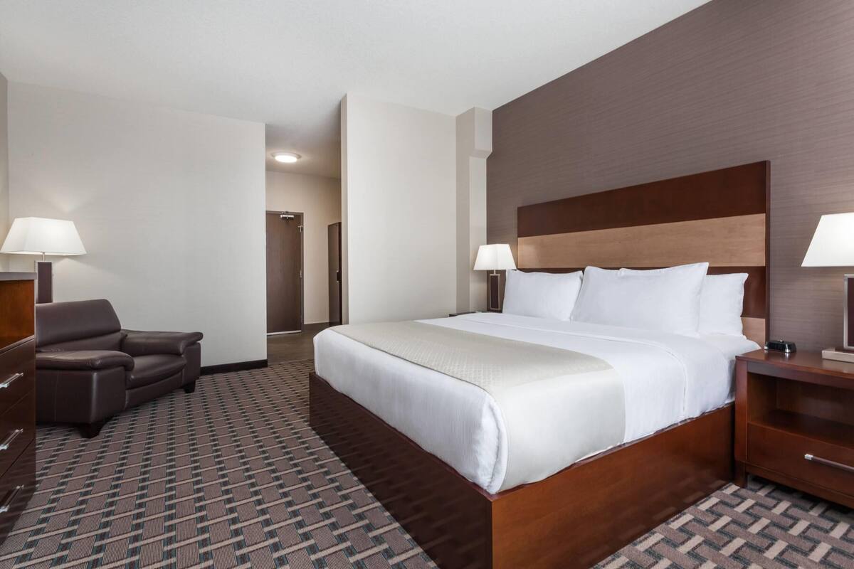 Habitación de hotel con una cama grande, dos mesitas de noche con lámparas, un sofá de cuero marrón y una alfombra estampada.