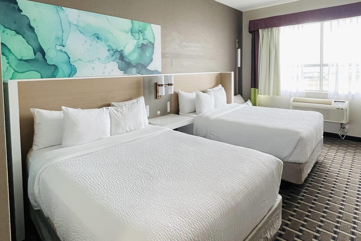 Habitación de hotel con dos camas, un cuadro abstracto grande en la pared, una ventana con cortinas y un suelo estampado.