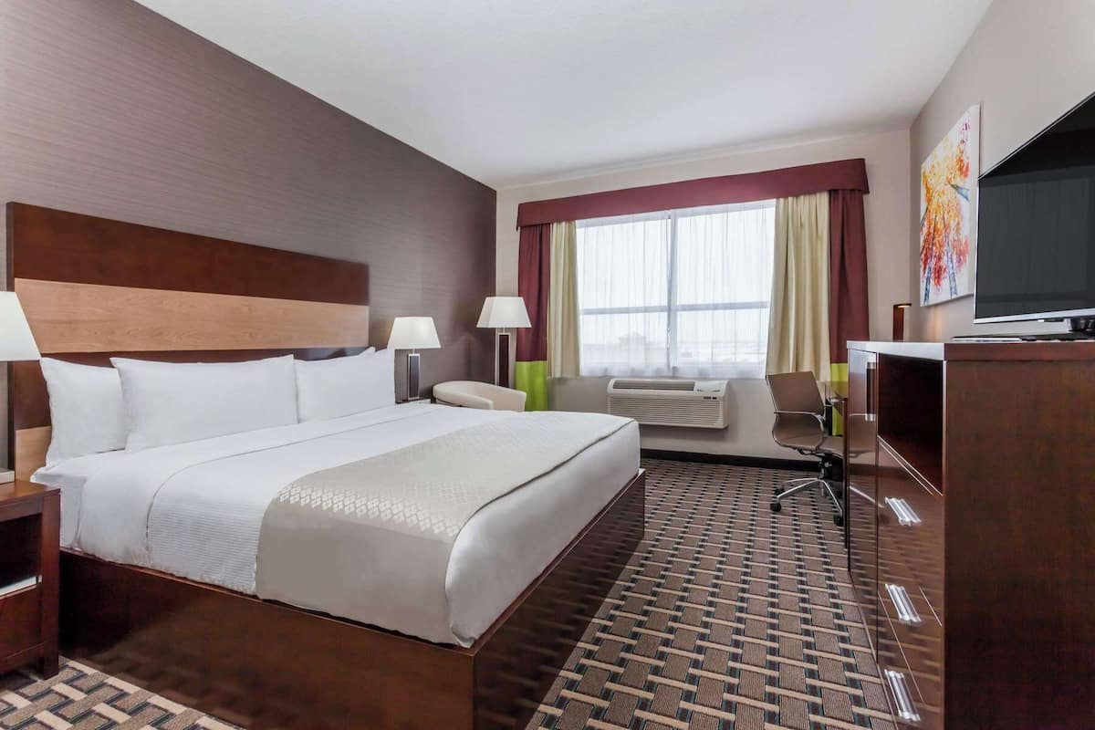 Habitación de hotel con una cama grande, dos mesitas de noche, un escritorio, una silla, un televisor y una ventana con cortinas.