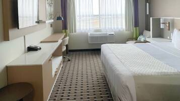Habitación de hotel con cama, escritorio, silla, televisor y ventana con cortinas.