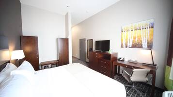 Habitación de hotel con una cama grande, un escritorio, una silla, un televisor y un cuadro en la pared.
