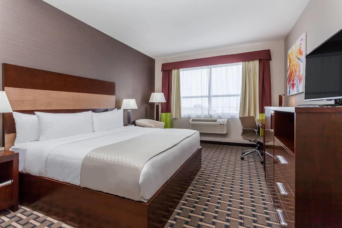 Una habitación de hotel con una cama grande, un escritorio, una silla, un televisor y una ventana con cortinas.