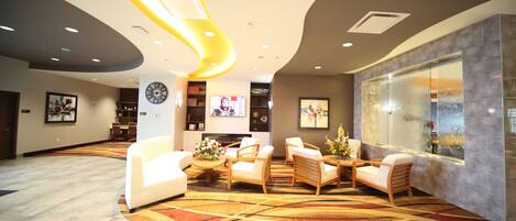 A modern lobby with a curved ceiling, recessed lighting, a clock, and a seating area with a floral centerpiece.