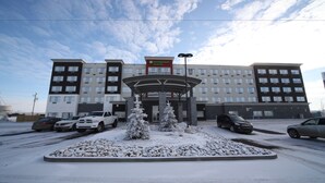 Un hôtel à plusieurs étages, doté d’une entrée centrale, d’un aménagement paysager recouvert de neige et de voitures garées.