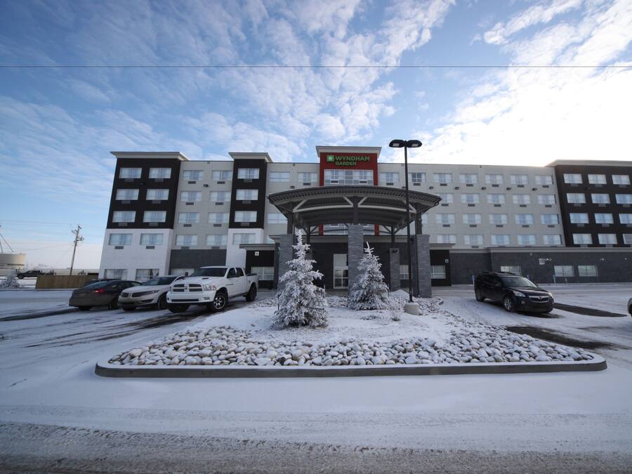 Hotel com vários andares, entrada central, paisagismo coberto de neve e carros estacionados.