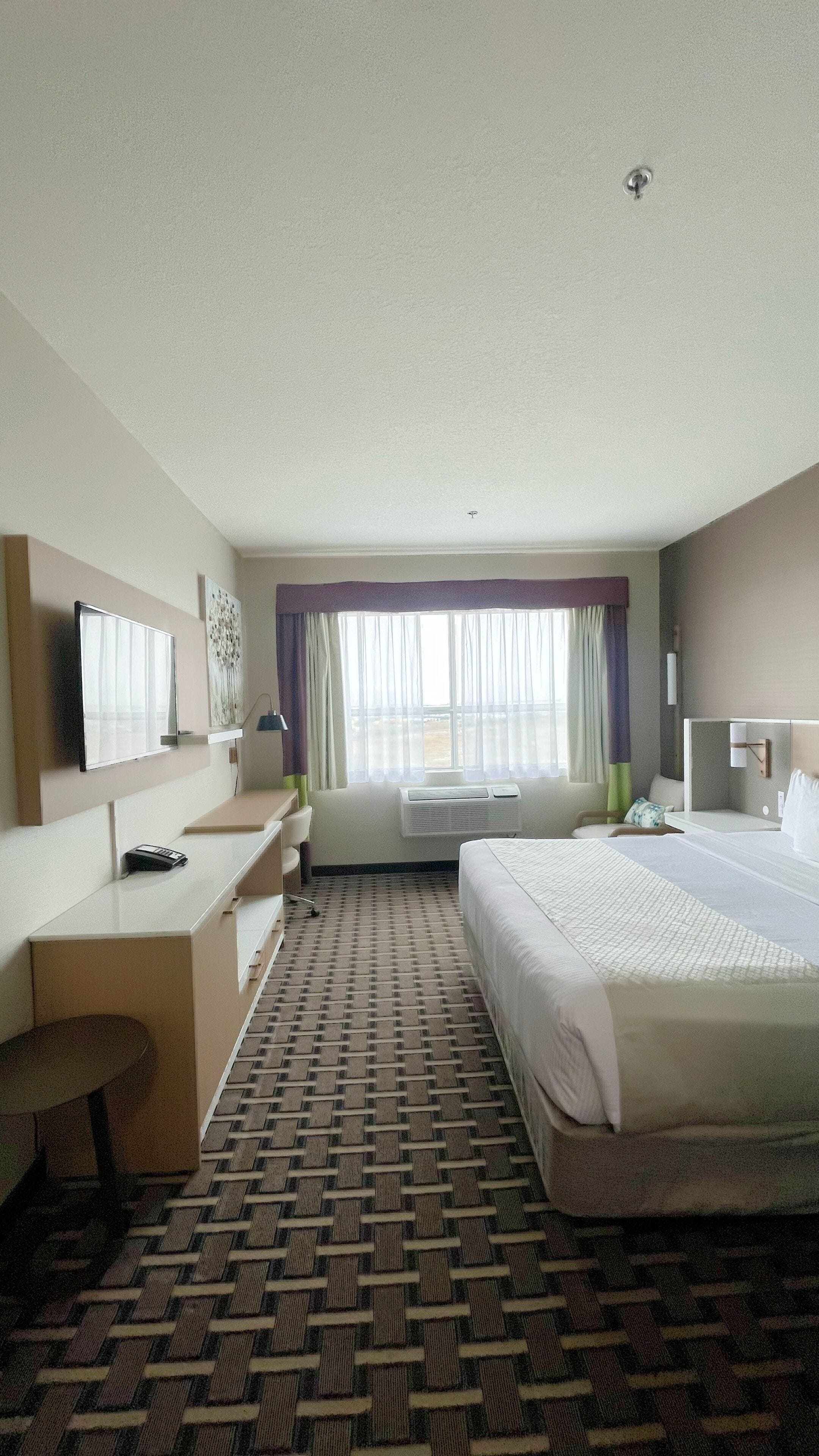 Habitación de hotel con cama, escritorio, silla y un ventanal con cortinas.