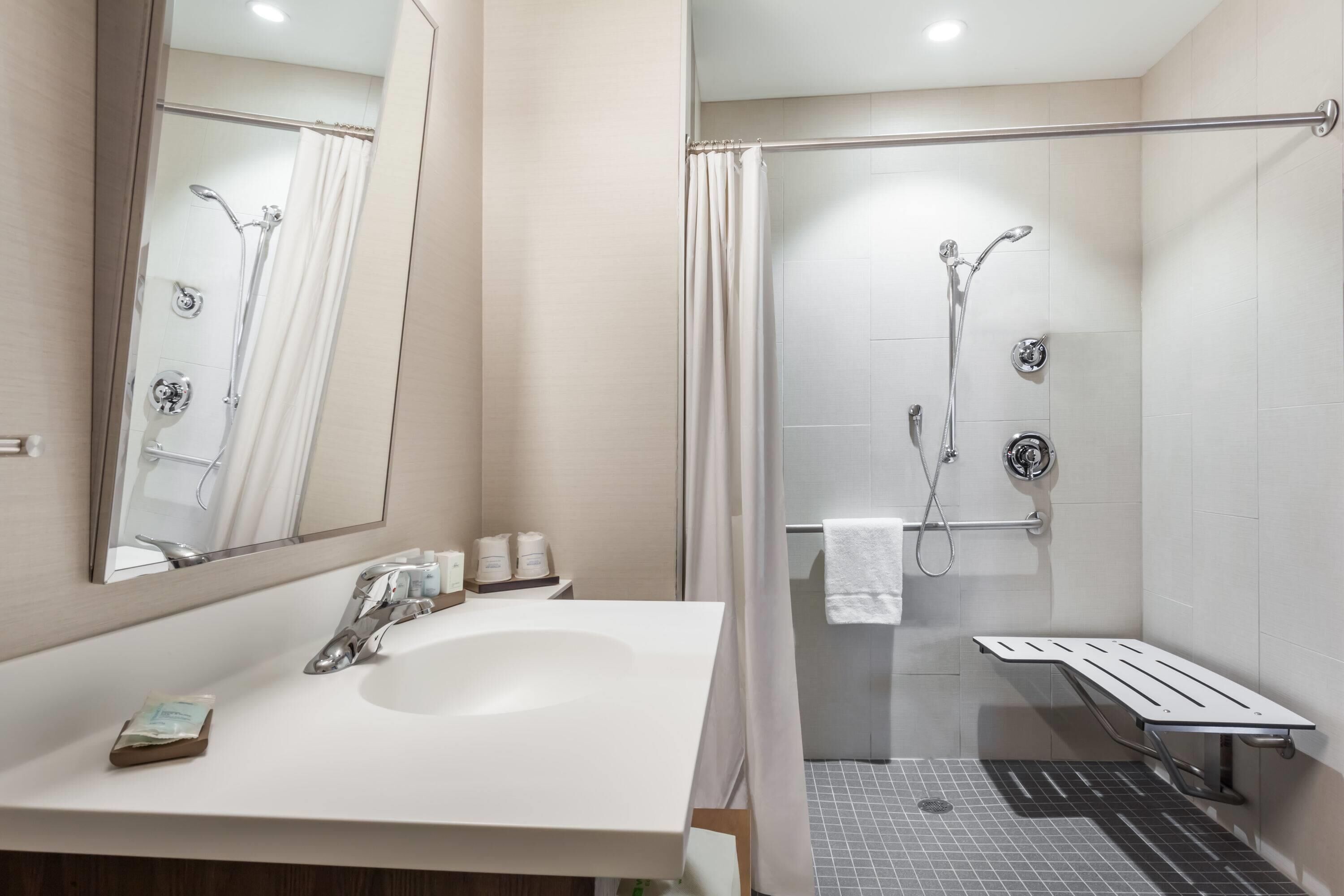 A bathroom with a white sink, a mirror, a shower with a glass door, and a bench.