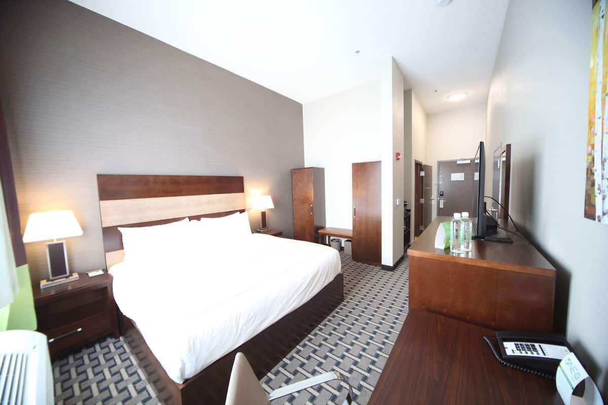 Habitación de hotel con una cama grande, mesitas de noche, un escritorio con una computadora, un televisor y la puerta del baño.