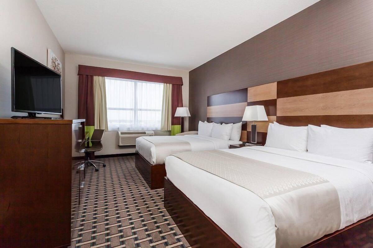 Habitación de hotel con dos camas, un escritorio con computadora, televisor y ventana con cortinas.