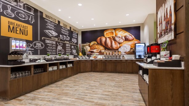 Un espace dédié au petit-déjeuner, avec un tableau affichant le menu, des machines à café et une variété d’aliments présentés sur le comptoir.
