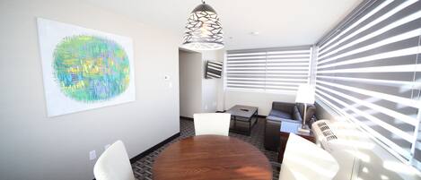 A conference room with a wooden table, white chairs, a hanging pendant light, and a large abstract painting on the wall.