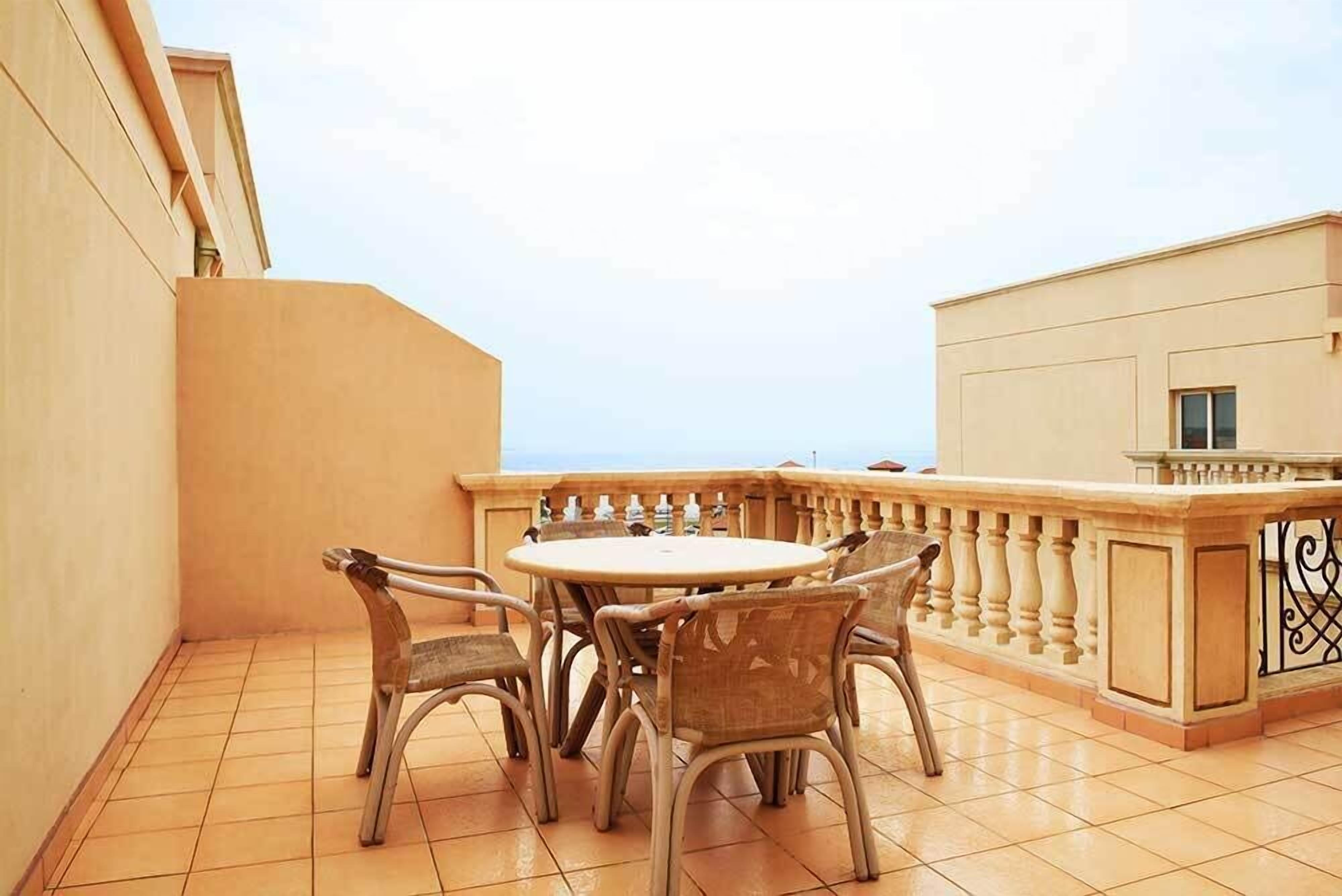 Ein Balkon mit rundem Tisch und Stühlen, einem Geländer und Blick zum Himmel.