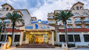 A hotel entrance with a prominent sign, a staircase leading up to the entrance, and palm trees in front. - Karan Sharq for Hotel Apartments Company (Al Jubail)