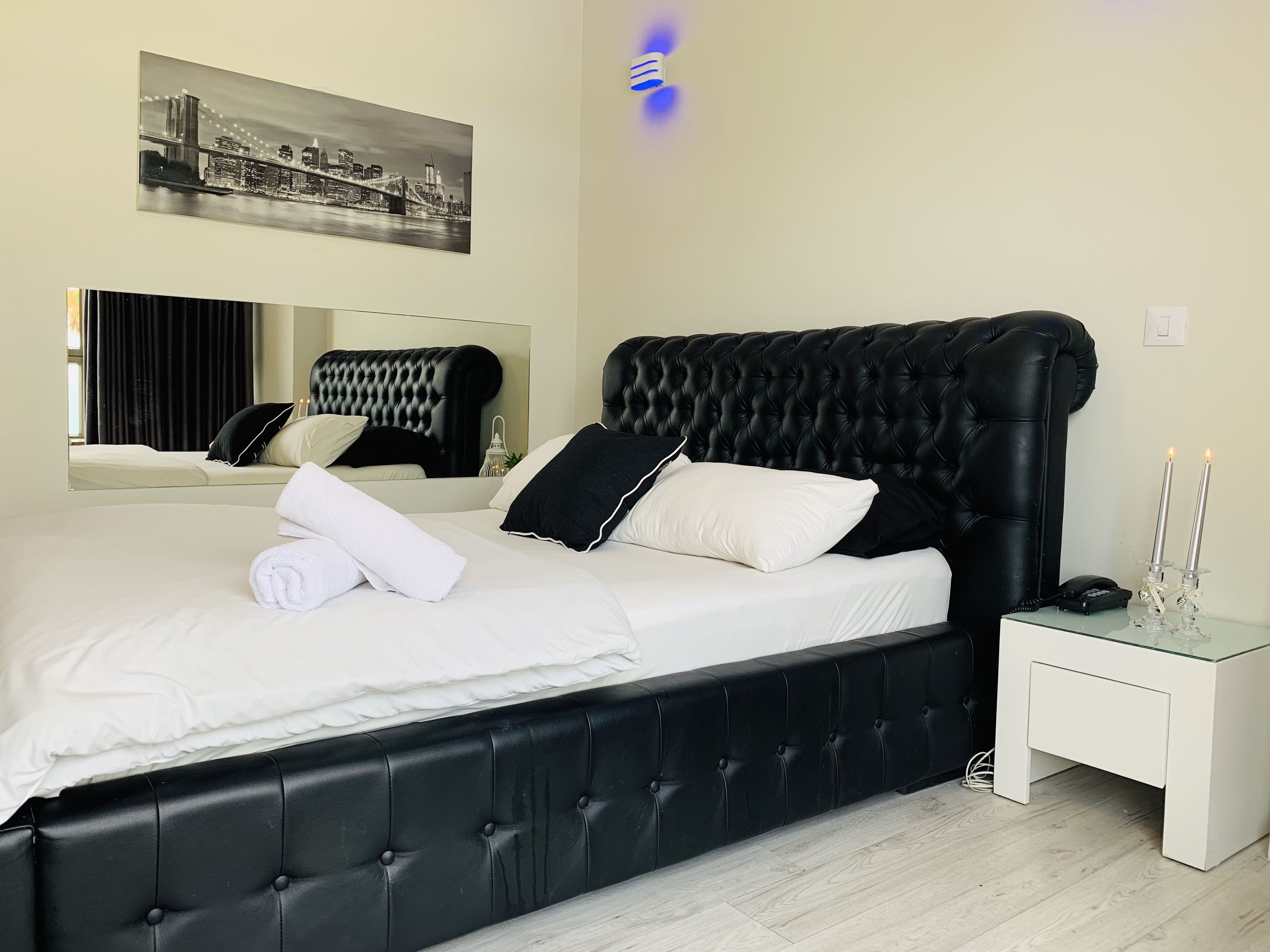 Un dormitorio moderno con un cabecero tapizado negro, ropa de cama blanca y una mesita de noche con lámpara.