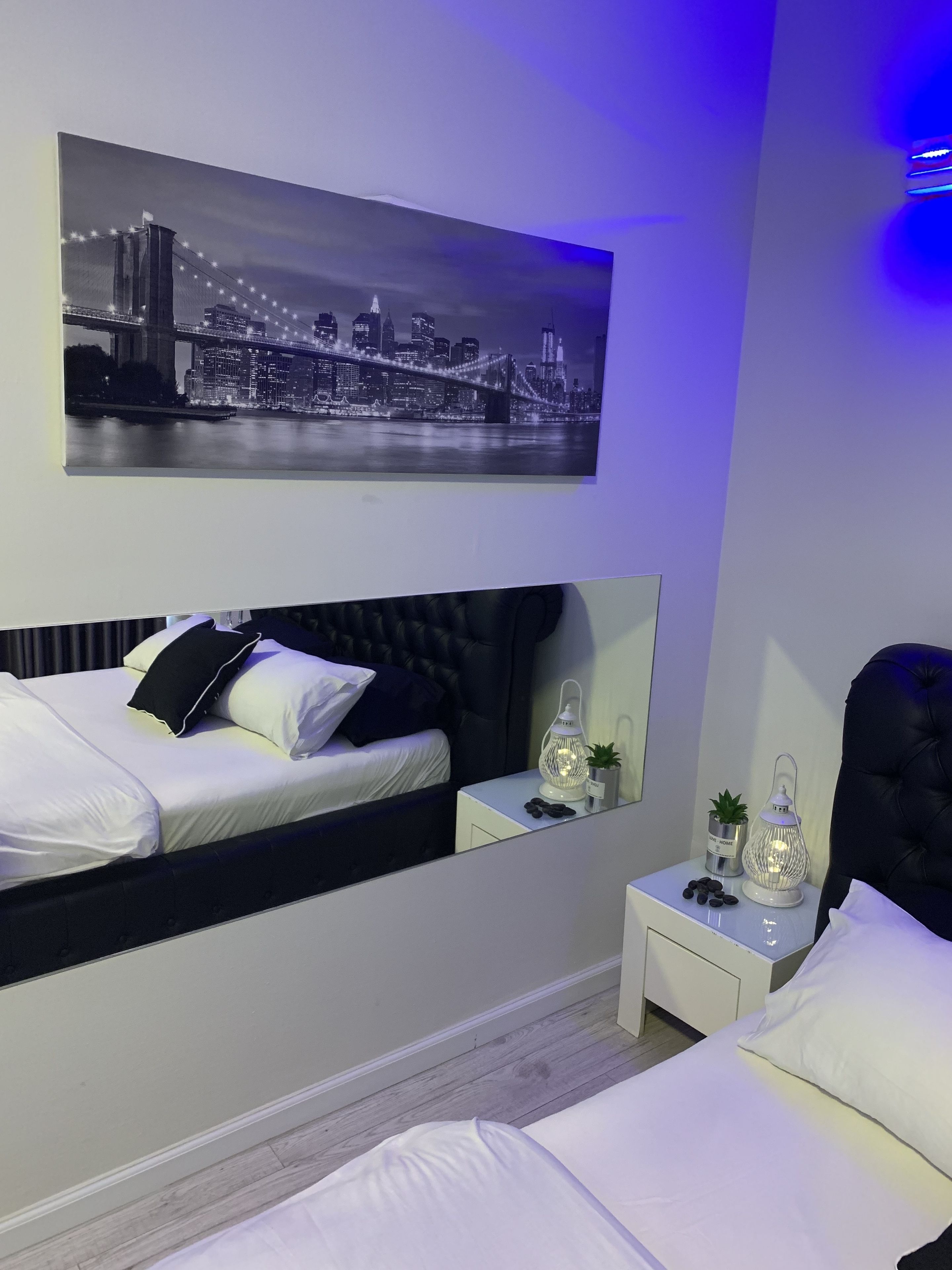 A modern bedroom with a bed, a nightstand with a lamp, and a cityscape painting above the bed.
