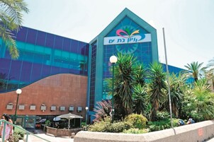 Un edificio moderno con un logotipo destacado en la fachada, rodeado de vegetación y palmeras.