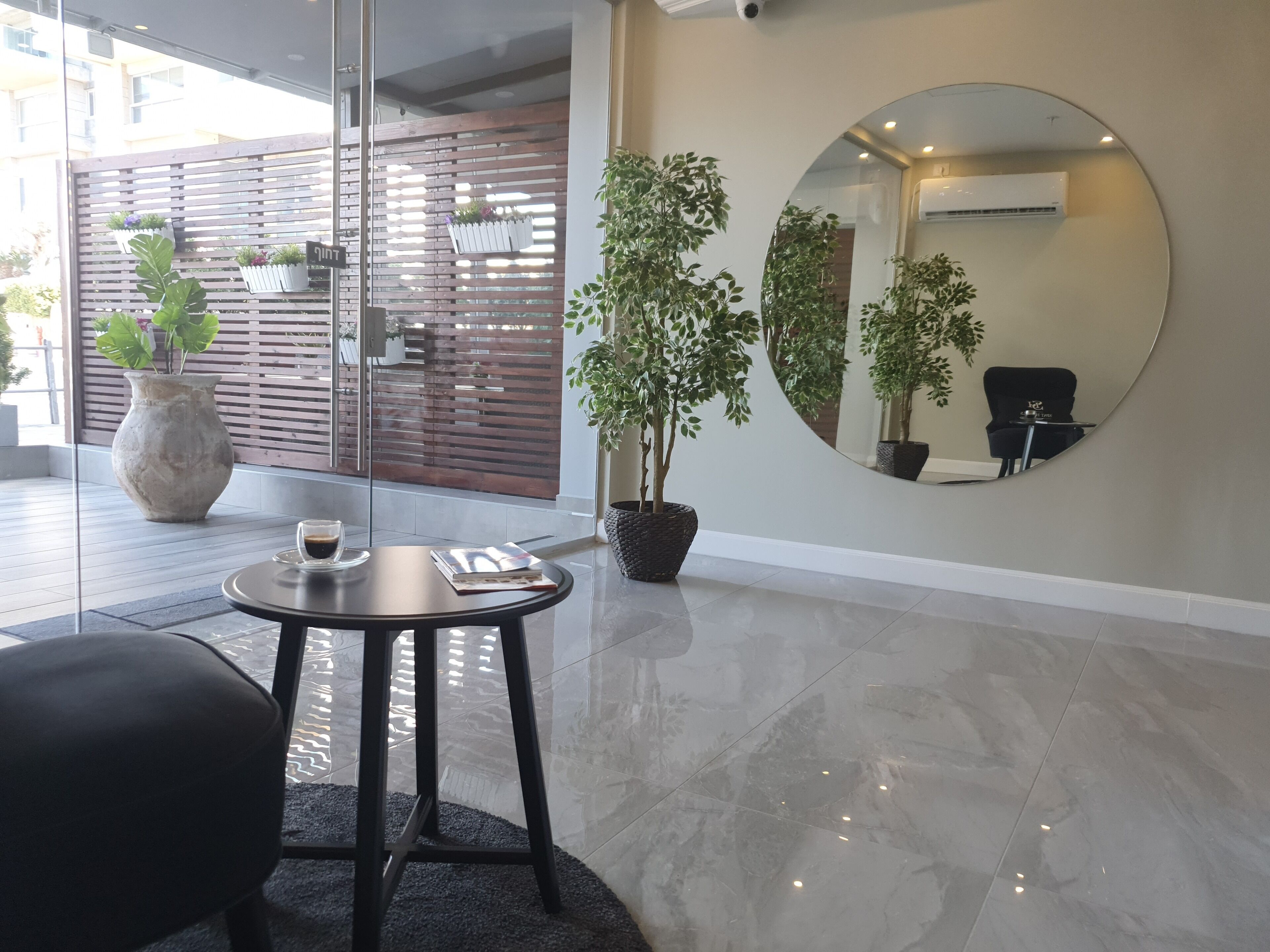 A modern reception area with a round mirror, a potted plant, and a table with a book and a cup.