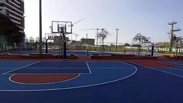 Una cancha de baloncesto al aire libre con superficie azul, un aro de baloncesto y una valla.