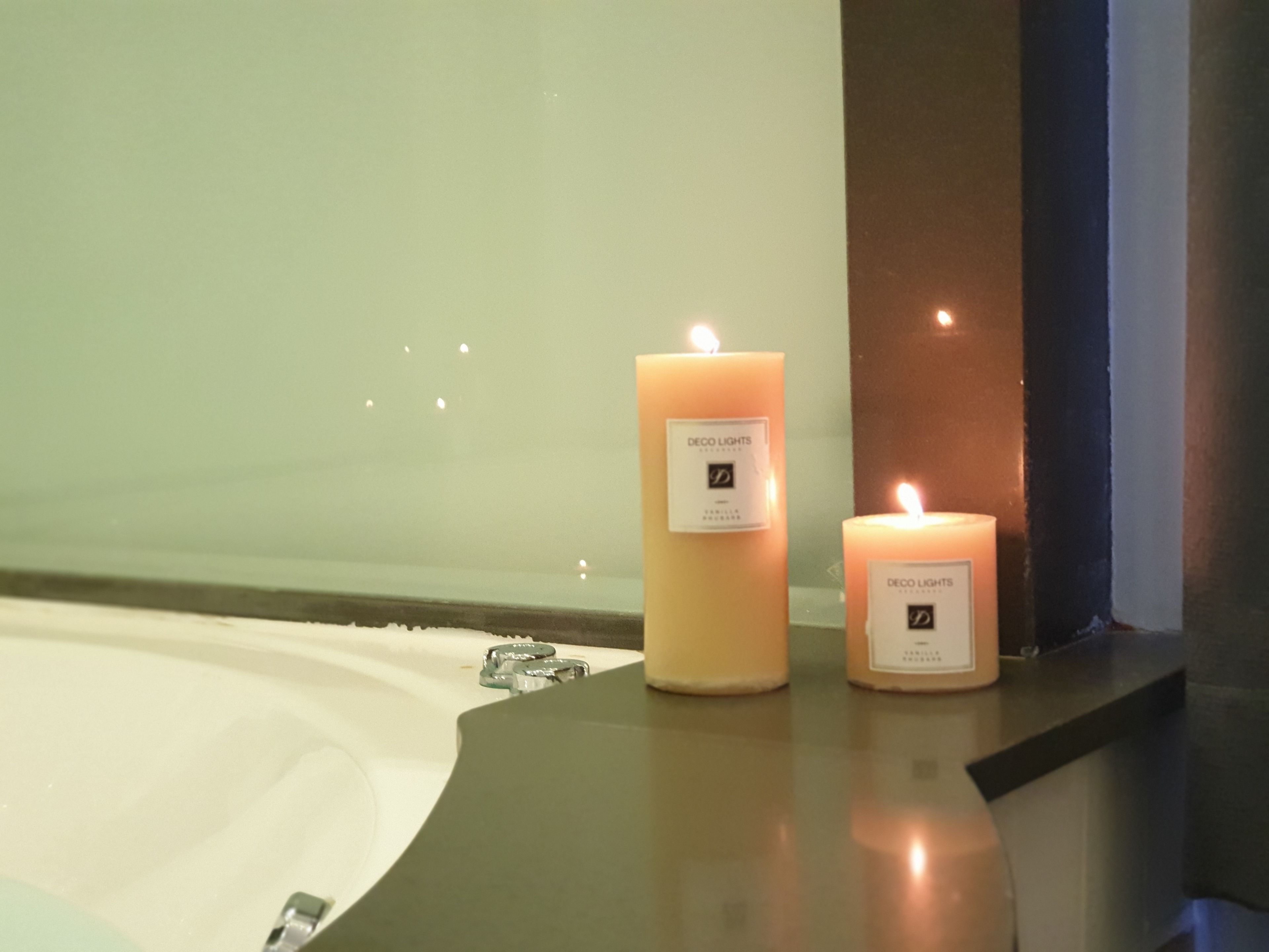 Dos velas encendidas sobre una encimera cerca de una bañera.
