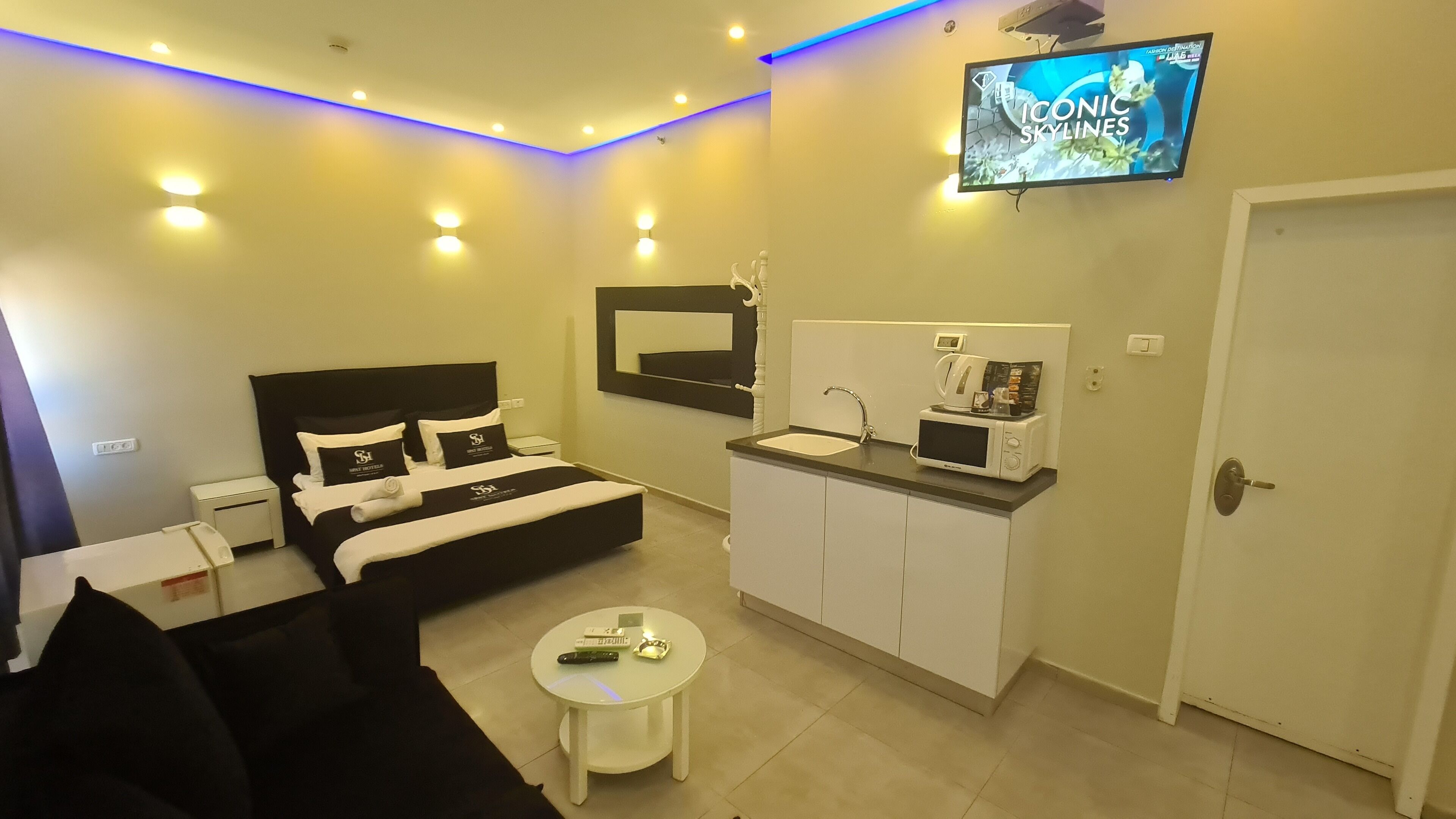 Ein modernes Hotelzimmer mit Bett, kleinem Schreibtisch, Sofa, Fernseher, Mikrowelle und Waschbecken.