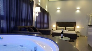 A modern hotel room with a large bathtub, a sofa, a bed, and two bedside tables with lamps.