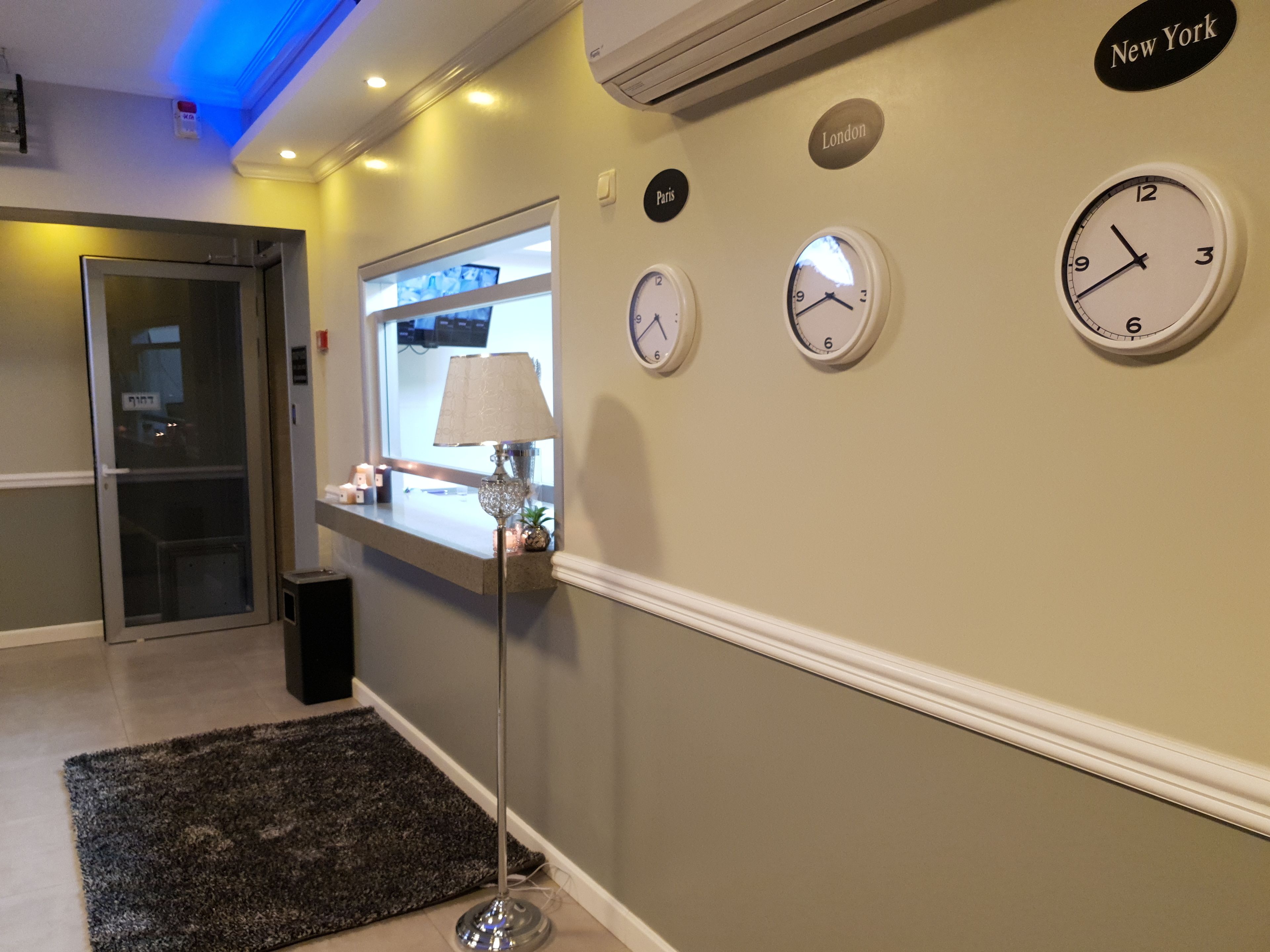 A hotel lobby with a reception desk, a floor lamp, and clocks indicating different cities.